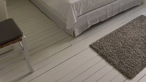 Una cama bien hecha con ropa blanca, dos mesitas de noche con lámparas, un cuadro enmarcado en la pared y una ventana con cortinas.
