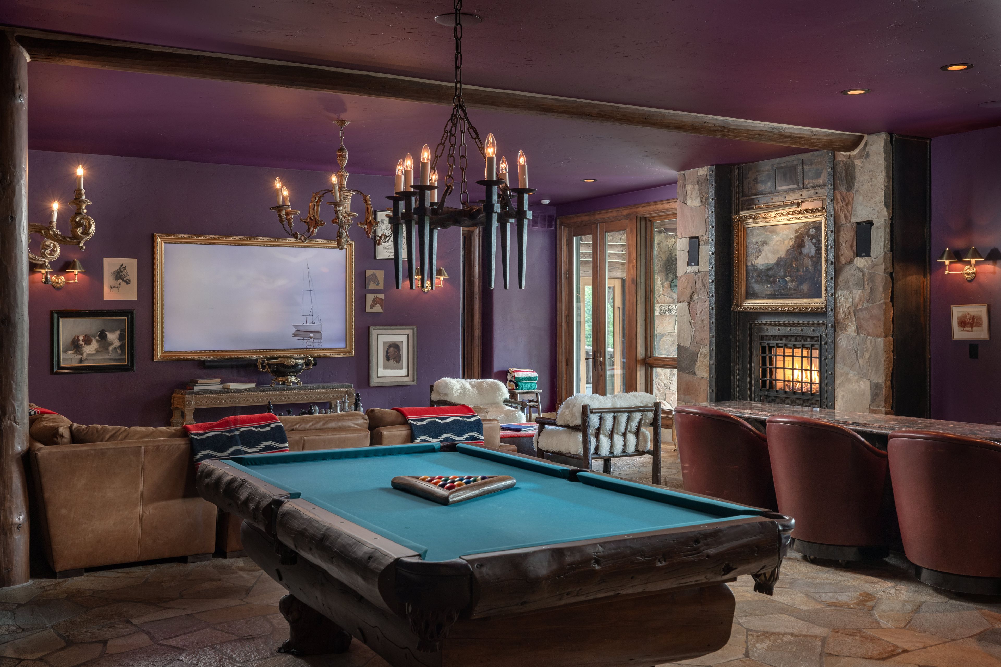A pool table in a room with purple walls, a chandelier, and a fireplace.