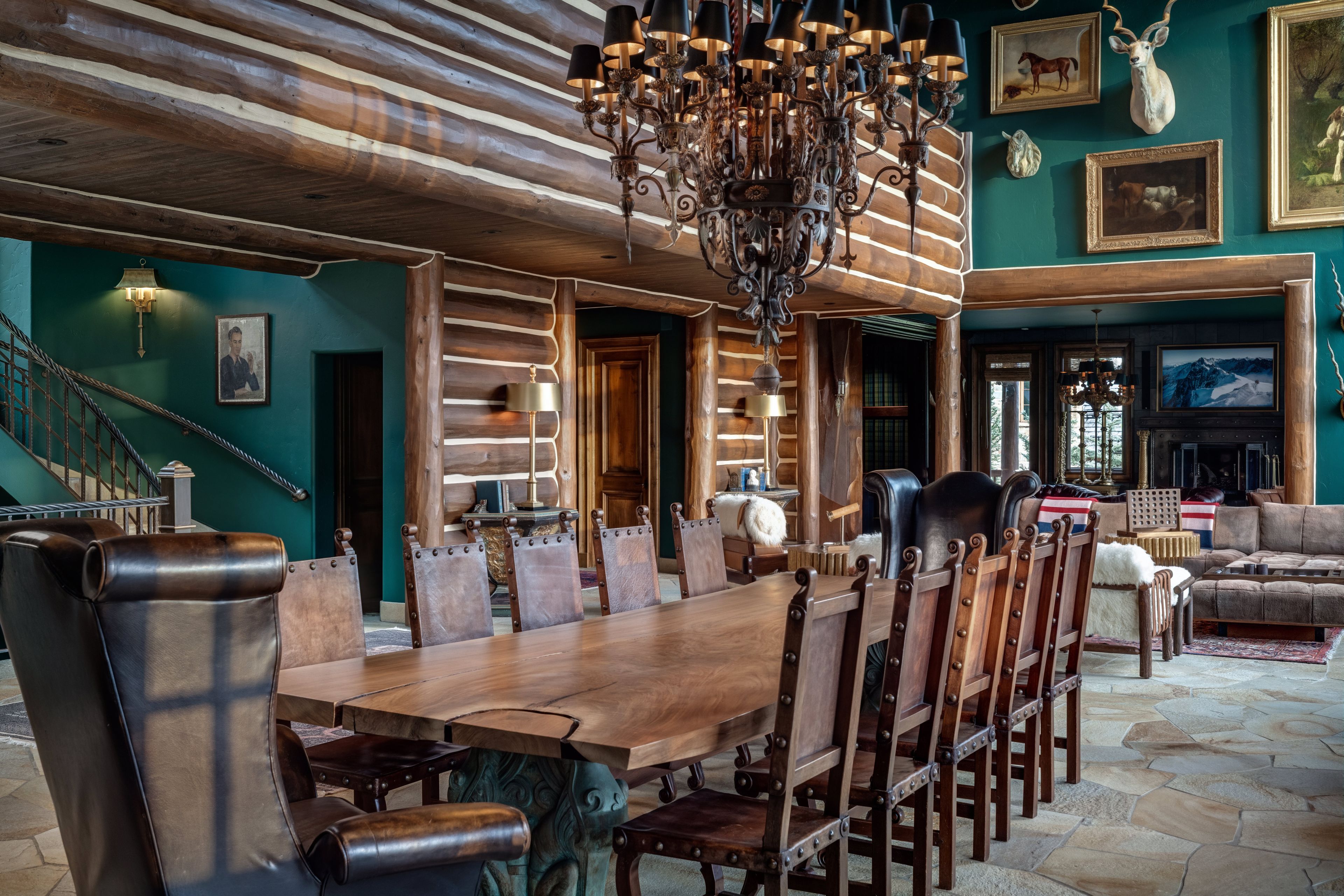 A spacious dining area with a large wooden table and chairs, a chandelier, and a staircase leading to another level.