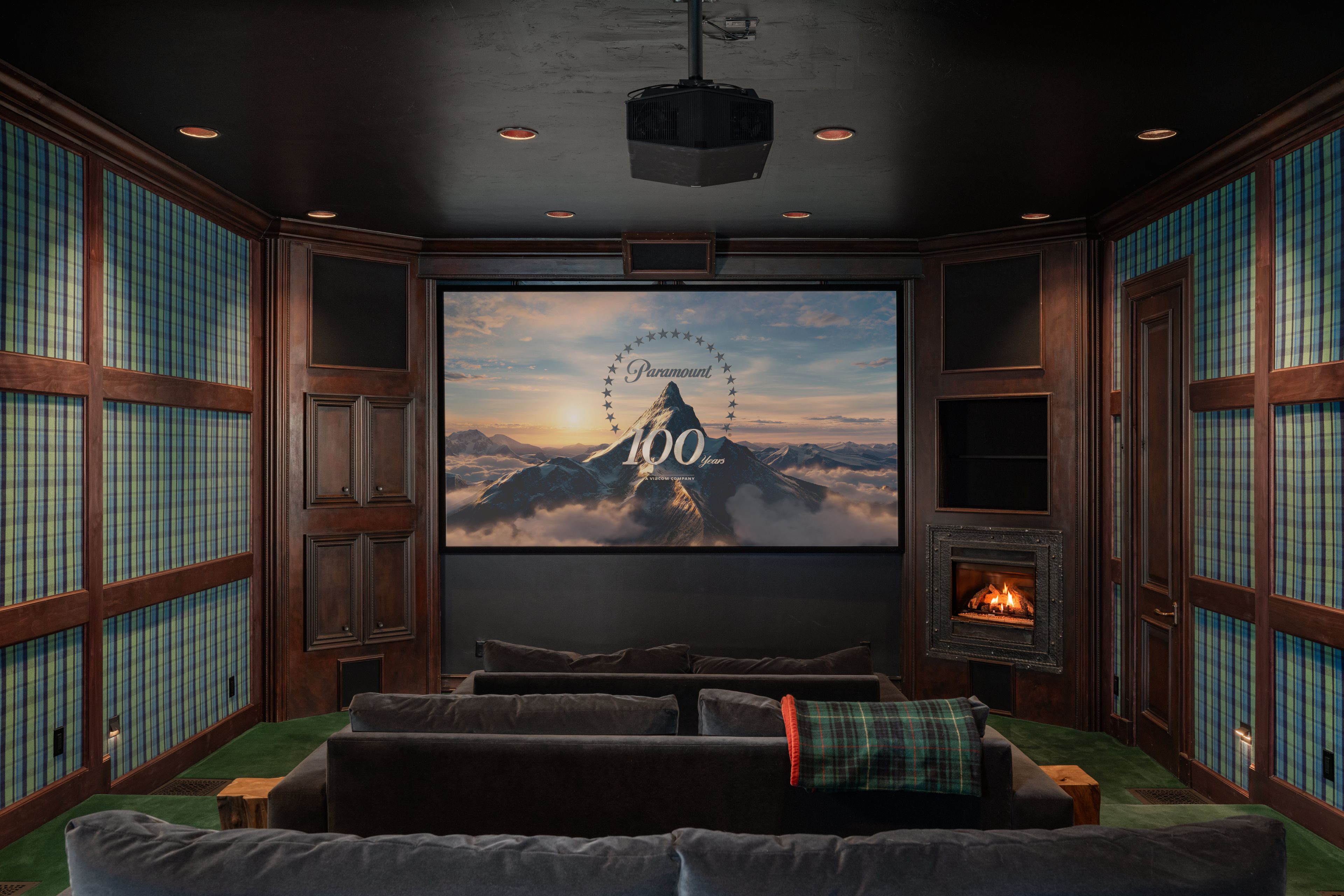 Une pièce chaleureuse avec un grand écran diffusant un paysage de montagne, une cheminée et un coin salon confortable.
