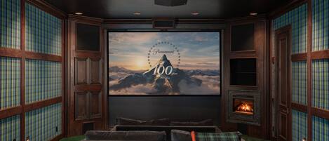 Une pièce chaleureuse avec un grand écran diffusant un paysage de montagne, une cheminée et un coin salon confortable.