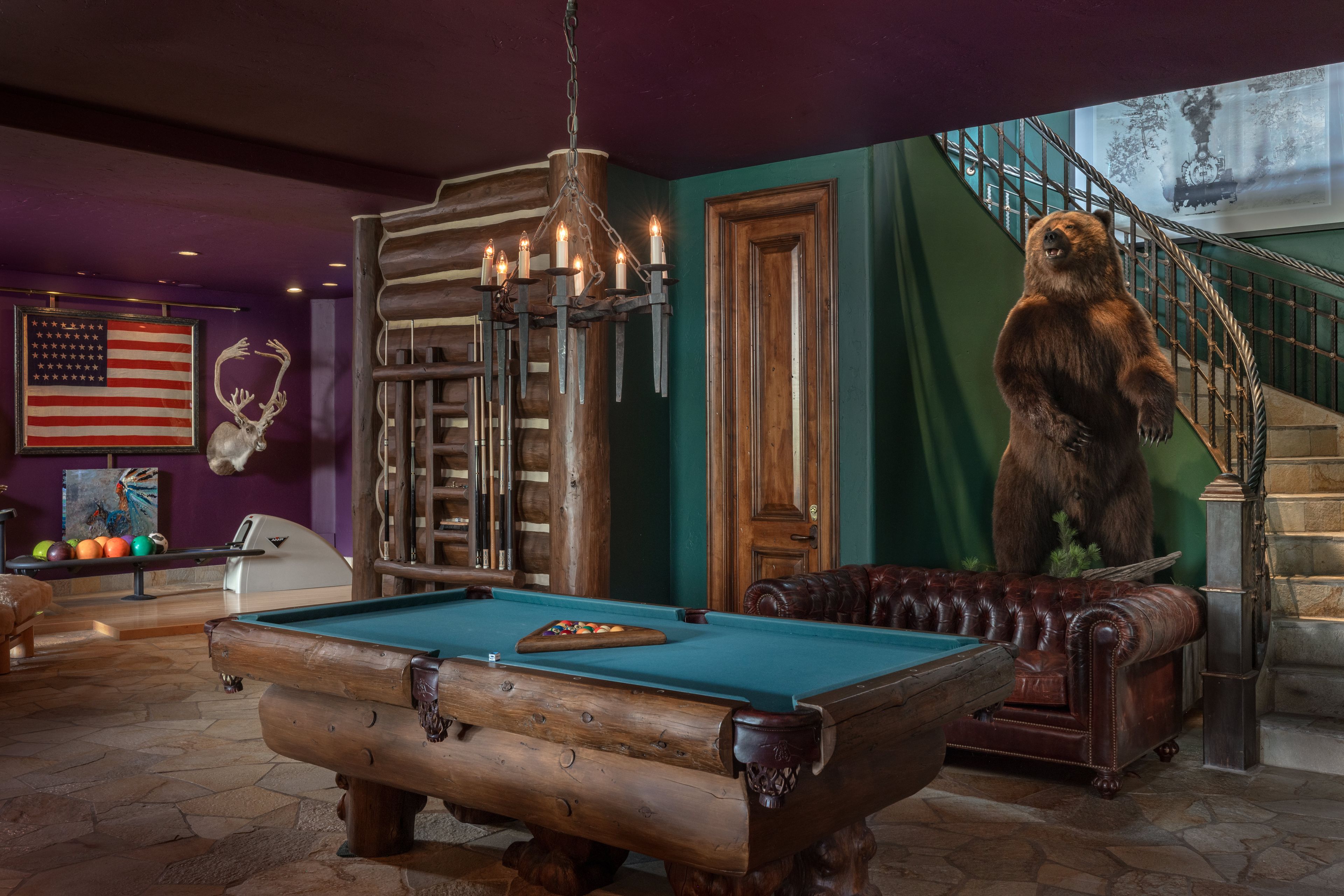 Een biljarttafel in een ruimte met een beerbeeld, houten meubels en een trap.