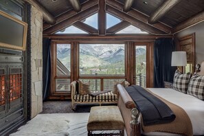 Ein Zimmer mit einem großen Bett, einer Sitzecke und Bergblick durch große Fenster.