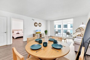 A modern living room with a round wooden dining table, wicker chairs, and a large window offering a view of the city. - Luxury Miami Brickell Stay-Bay View (Miami)