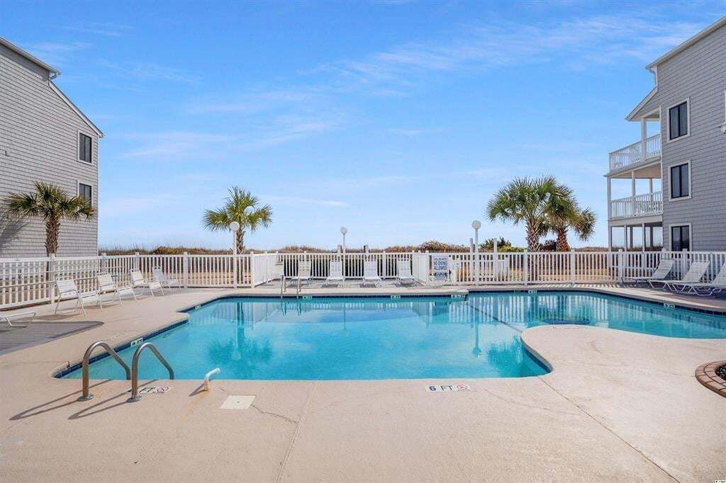 A swimming pool with lounge chairs and palm trees, surrounded by a fence.