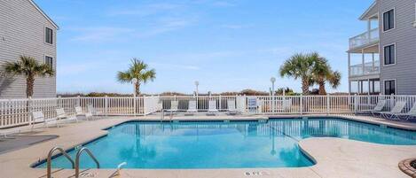 A swimming pool with lounge chairs and palm trees, surrounded by a fence.