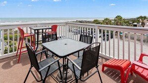 Ein Balkon mit Tisch und Stühlen, der Blick auf einen Strand und den Ozean freigibt.