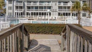 Ein mehrstöckiges Hotel mit Balkonen, einem Pool und einer Holzterrasse, die zum Eingang führt.