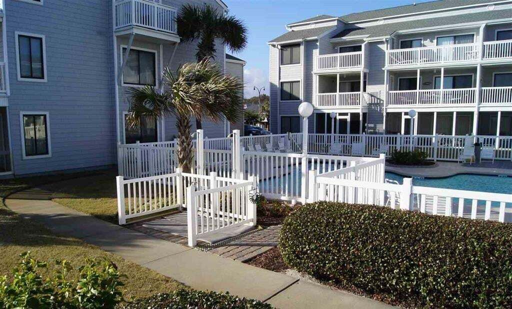 A multi-story hotel with balconies, a swimming pool, and a white fence.