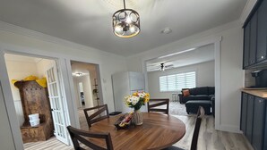 Un coin repas avec une table en bois, des chaises et un vase de fleurs. Il y a également un coin cuisine avec des placards et un ventilateur de plafond.