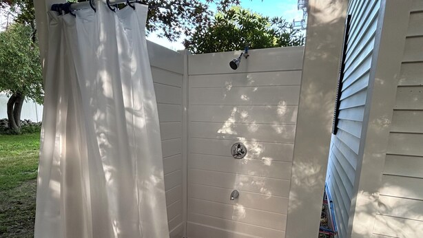 A wooden deck with a white shower enclosure, a curtain, and a metal shower head. - Queens Way Retreat-12 Guests-Pet Friendly (Wells)