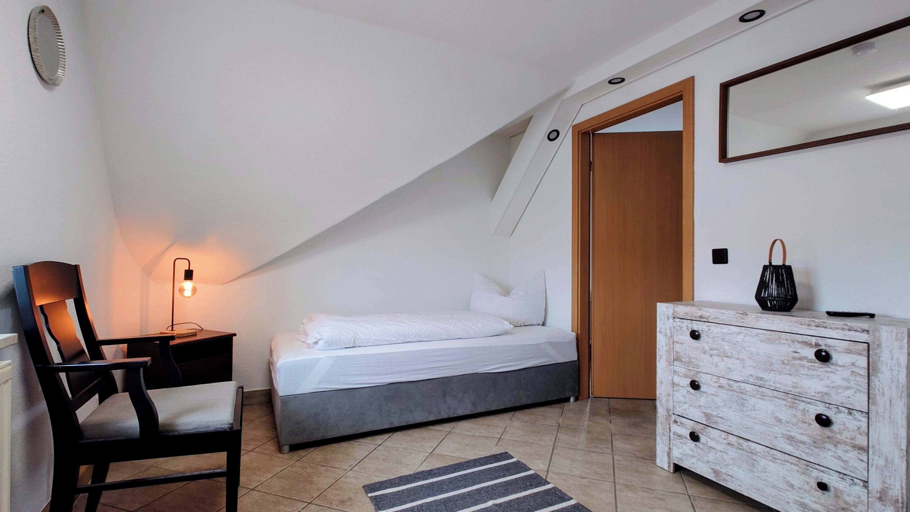 A bedroom with a bed, a desk with a lamp, a dresser, and a mirror.