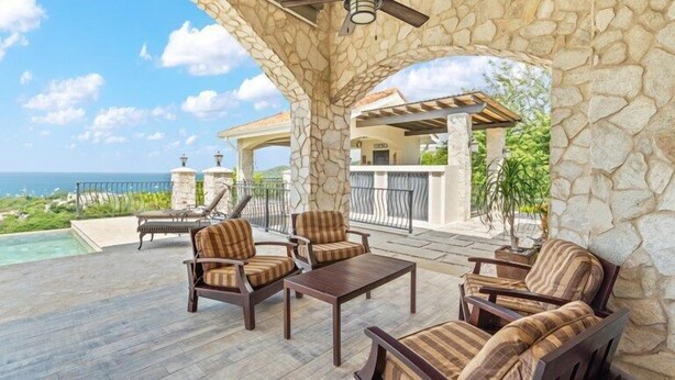 A stone-covered patio with outdoor furniture, a ceiling fan, and a view of the ocean.