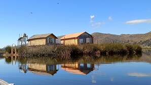 Ett hus vid sjön med en brygga, en liten båt och ett berg i bakgrunden.