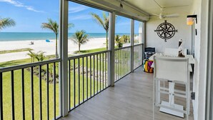 Un balcon avec vue sur la plage, une décoration murale en forme de boussole et une table blanche avec une chaise.