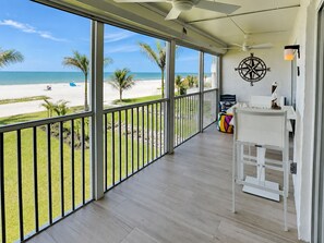 A balcony with a view of the beach, a compass wall decoration, and a white table with a chair. - Pointe South 107 | Stunning Views + Resort Pool (Fort Myers Beach)