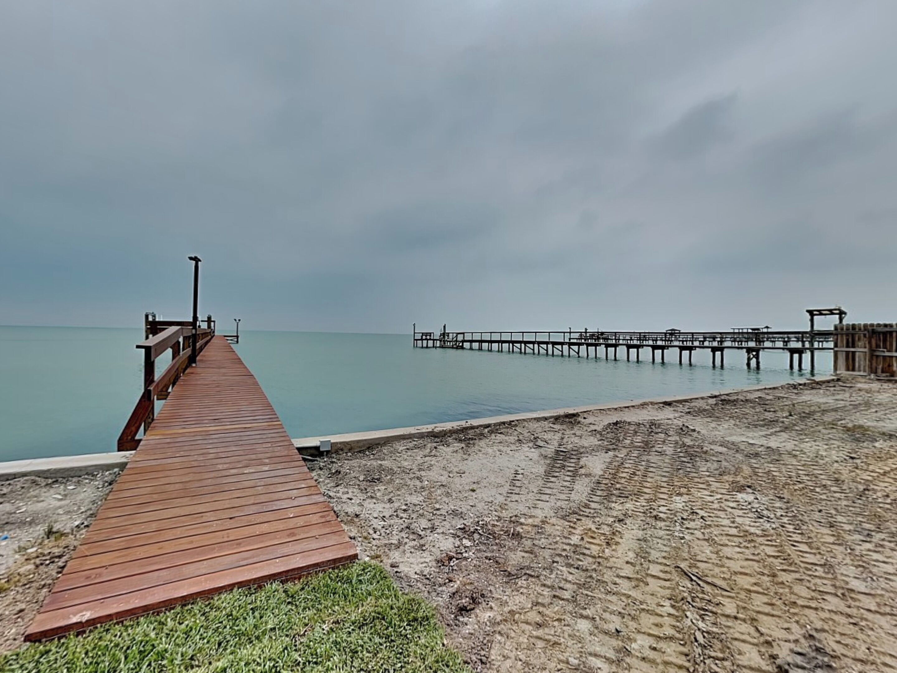 A wooden pier extending into calm waters, a sandy beach, and a distant pier structure.