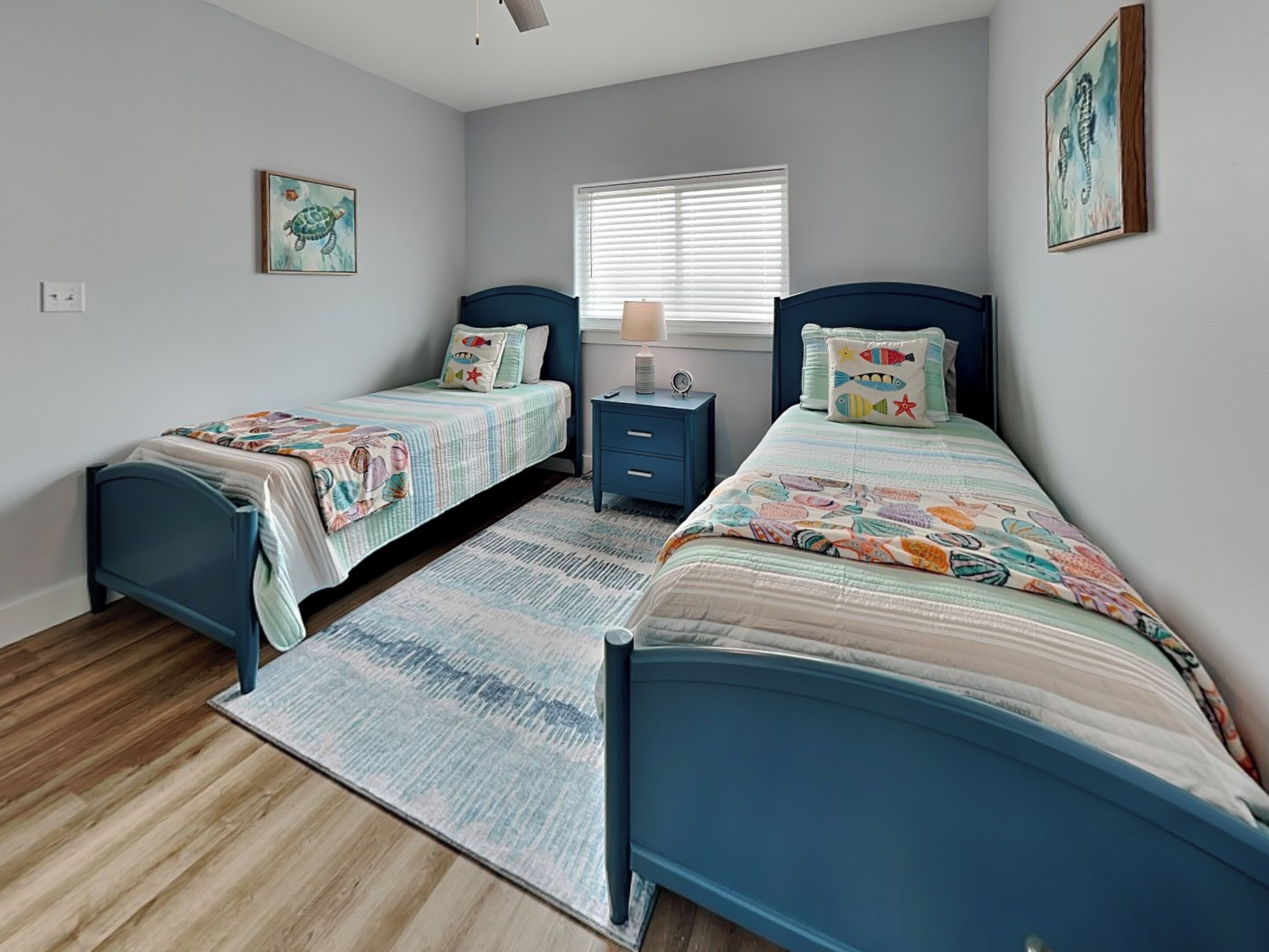 A bedroom with two beds, a nightstand, a window with blinds, and a rug.