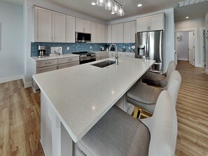Una cocina moderna con armarios blancos, un refrigerador de acero inoxidable y una isla central con taburetes de bar.