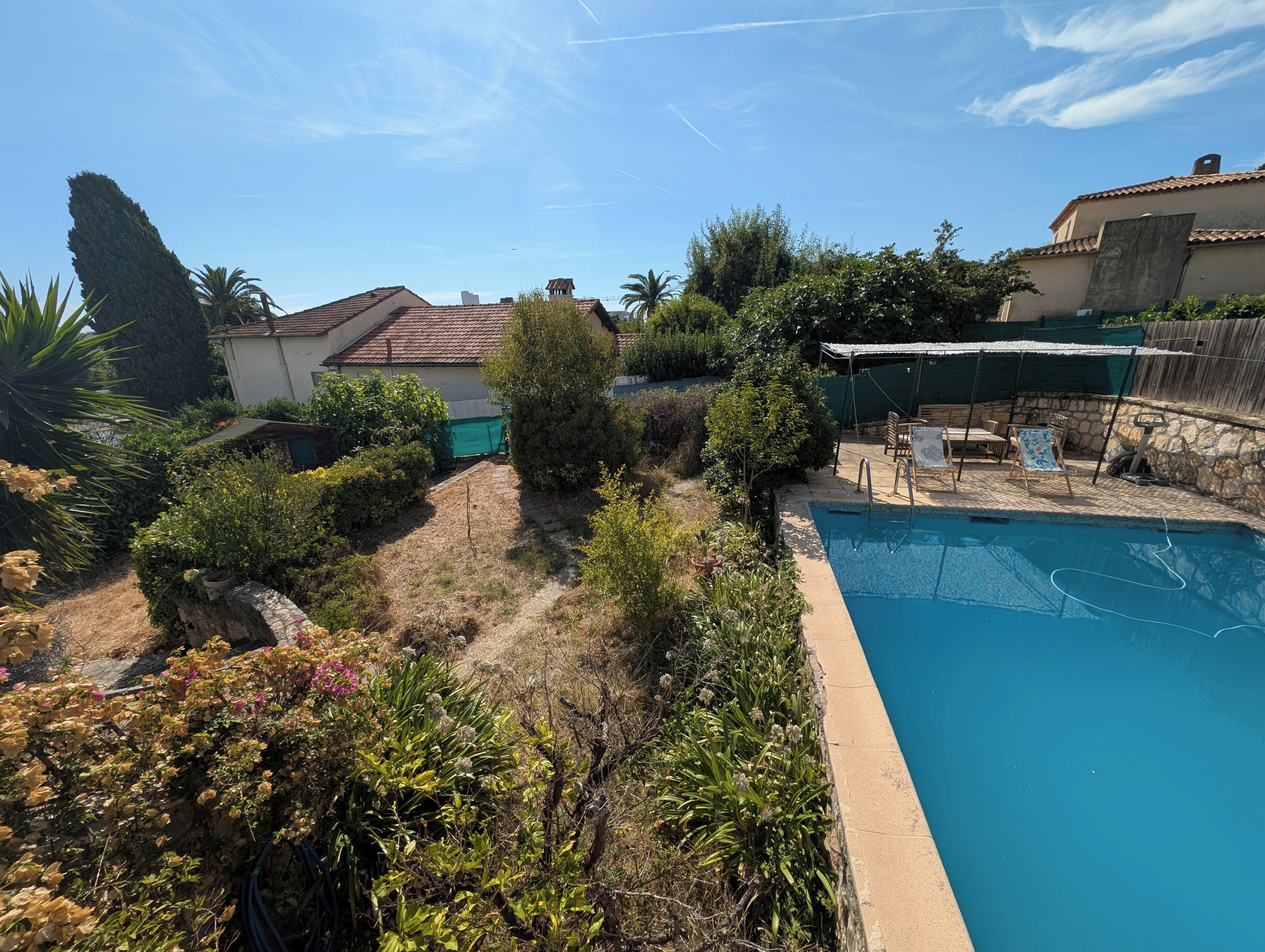 Une piscine dotée d’une plage en pierre, entourée de verdure et surplombée par un ciel dégagé.