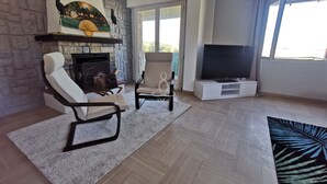 Ein Wohnzimmer mit Kamin, zwei Sesseln, einem Fernseher und einem großen Fenster.