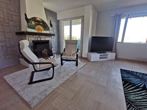 Ein Wohnzimmer mit Kamin, zwei Sesseln, einem Fernseher und einem großen Fenster.