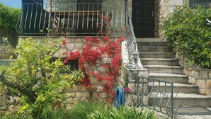 Ein Steinhaus mit Balkon, einer Treppe und einem Garten mit roten Blumen.
