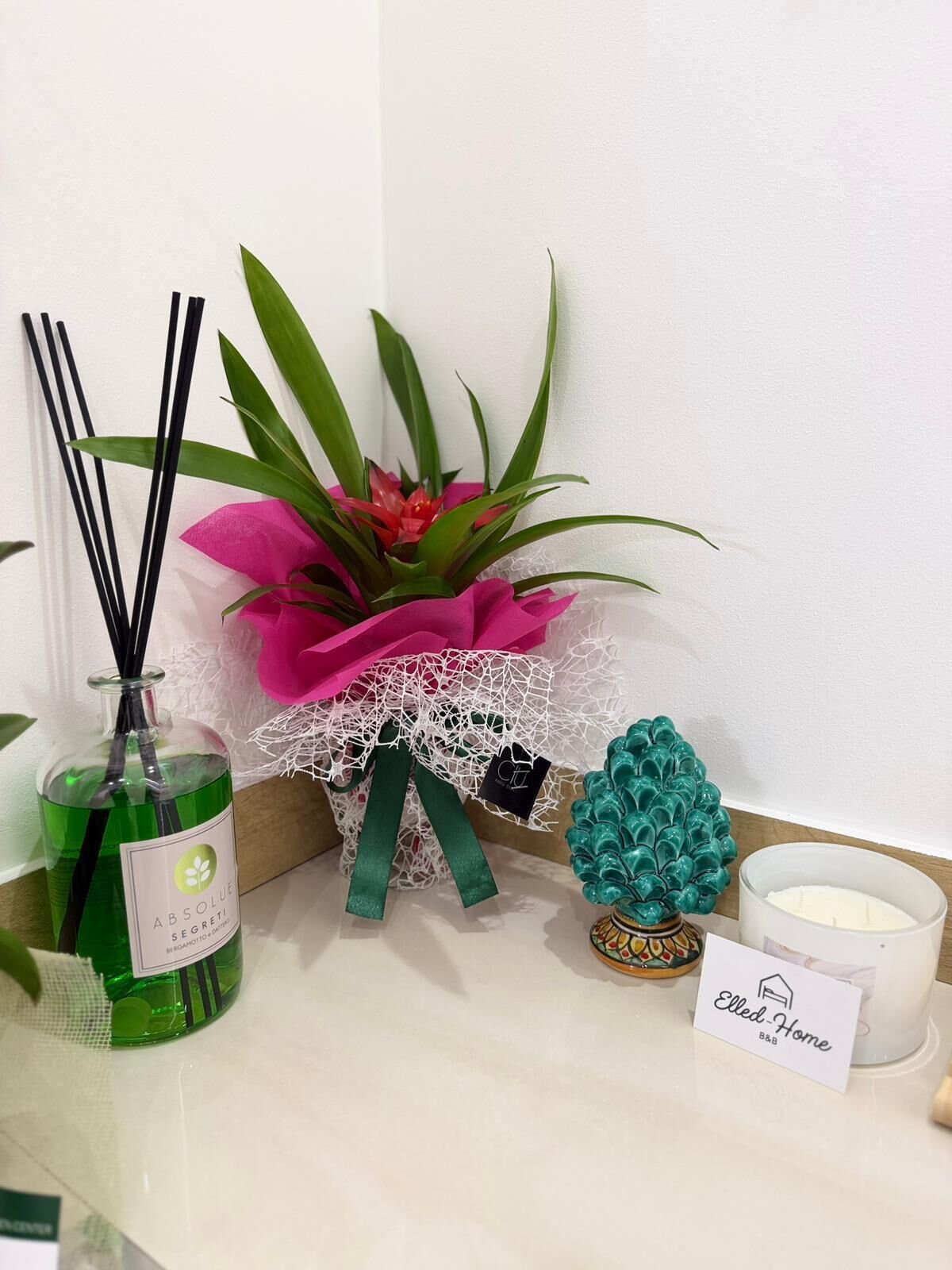 A table with a green bottle, a pink flower arrangement, a teal decorative item, and a candle labeled 'Elled-Home.'