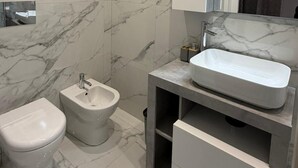 A modern bathroom with a marble floor, a bidet, a toilet, and a vanity with a sink. - Elled-home (Misterbianco)