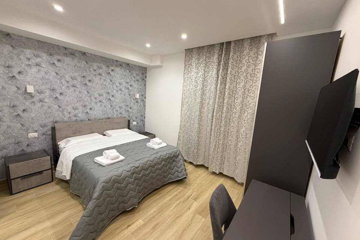 A modern bedroom with a large bed, a desk, and a television.