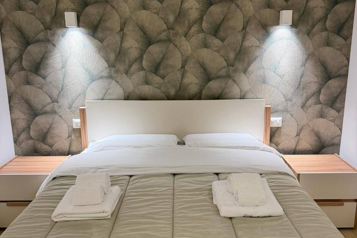 A neatly made bed with two pillows, a headboard, and two bedside tables with lamps.