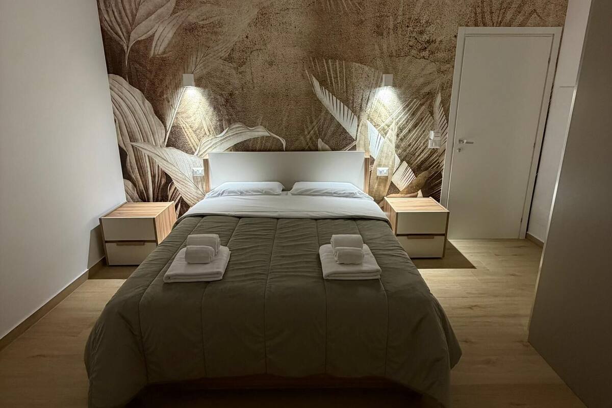 A modern bedroom with a large bed, two bedside tables, a headboard, and a wall mural.