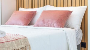A bed with white and pink pillows, a beige blanket, and a wooden headboard. - Marina Legacy I Boutique Residence (Faro)