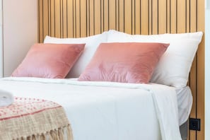 A bed with white and pink pillows, a beige blanket, and a wooden headboard. - Marina Legacy I Boutique Residence (Faro)