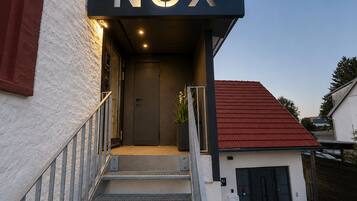 Een moderne gevel met een 'NOX' bord, een trap en een klein bijgebouw met een rood dak.