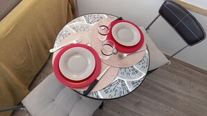 Ein runder Tisch mit einer gewebten Tischunterlage, zwei weiße Teller mit roten Rändern und ein schwarzer Stuhl.