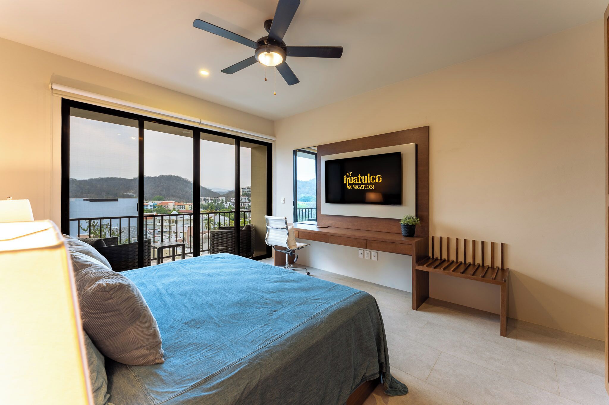 Une chambre avec un lit, une télévision, un balcon avec vue et un ventilateur de plafond.
