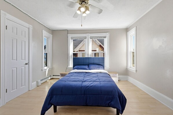 A bedroom with a bed, a ceiling fan, and a window with a view.