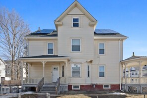 A two-story house with a front porch, a small attached garage, and solar panels on the roof.
