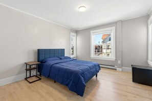 A bedroom with a bed, a nightstand, a window, and a view of buildings outside.