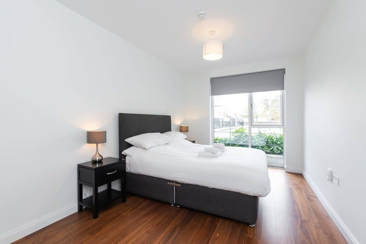 Quarto moderno com cama, mesas de cabeceira e janela com vista.