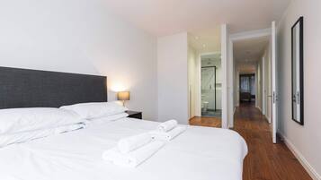 Una habitación de hotel con una cama bien hecha, una mesita de noche con una lámpara y un pasillo que lleva a un baño.