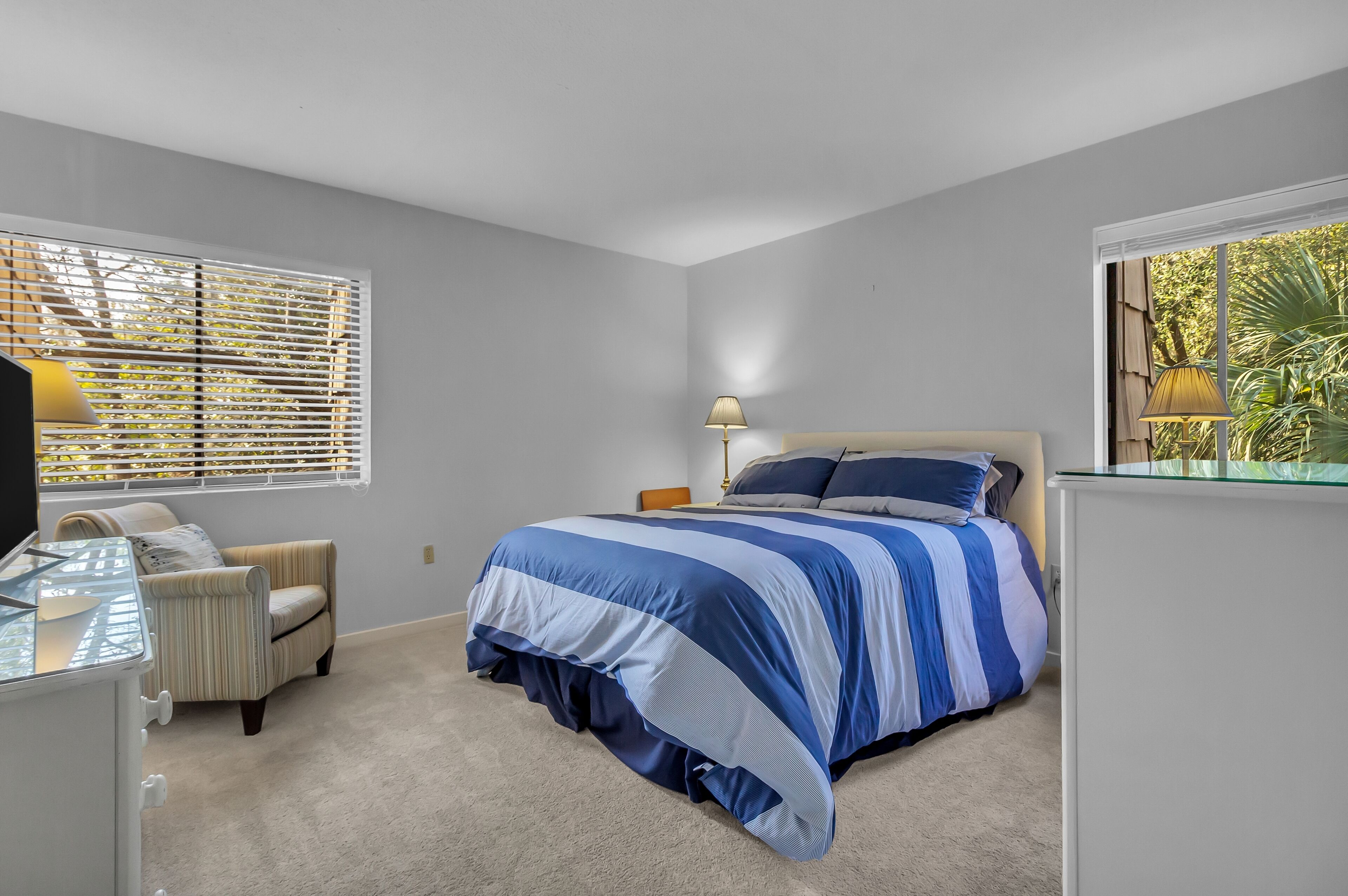 A bedroom with a bed, a chair, a desk, and a window with blinds.