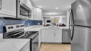Una cocina moderna con electrodomésticos de acero inoxidable, armarios blancos y salpicadero de azulejos azules.