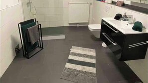 Un bagno moderno con doccia, WC e lavandino, caratterizzato da un soffitto illuminato di verde e un tappeto a righe.