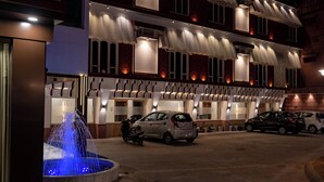 Un hotel con una fuente, coches aparcados y una fachada bien iluminada.