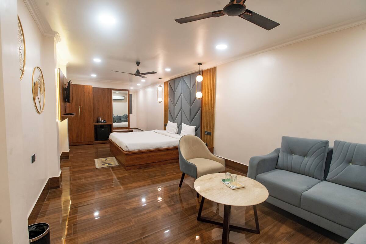 Une chambre d’hôtel équipée d’un lit, d’un canapé, d’une chaise, d’une petite table, d’un ventilateur de plafond et d’un téléviseur fixé au mur.