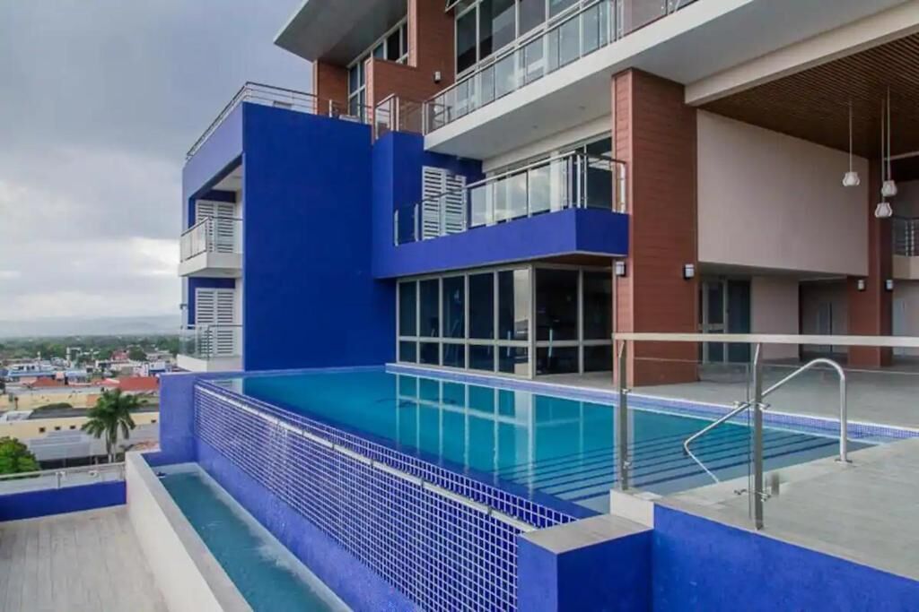 A modern building with a blue exterior, a swimming pool, and a view of the cityscape.