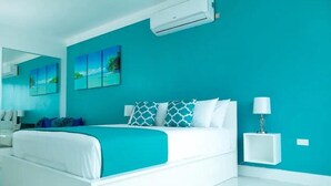 A modern bedroom with a white bed, teal walls, and a small bedside table with a lamp. - City Apartment in Kingston AC with Pool (Kingston)