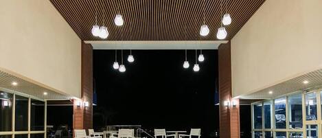 An indoor seating area with tables and chairs, a wooden slatted ceiling, and hanging pendant lights.
